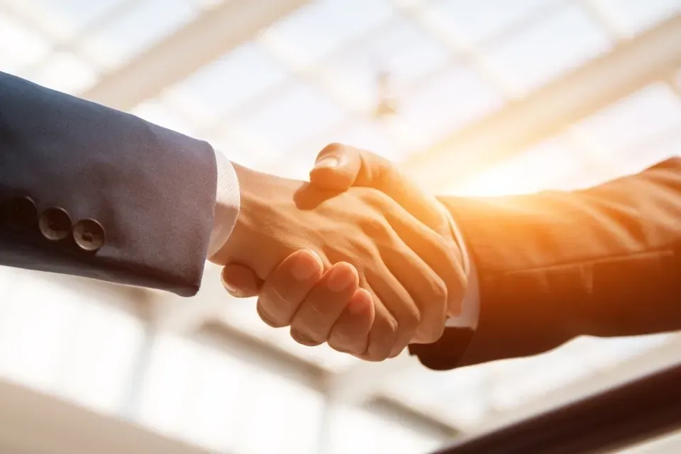 Two people shaking hands in a room with sunlight coming through the window.