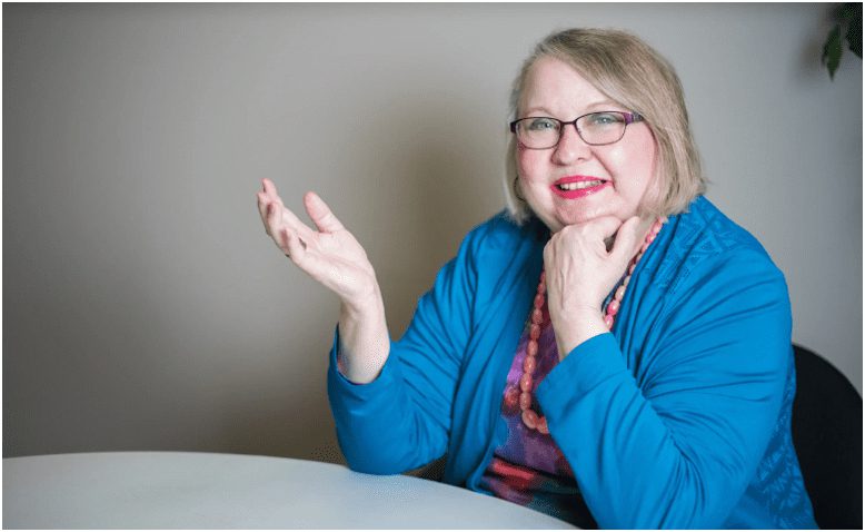 A woman sitting at a table with her hand raised.