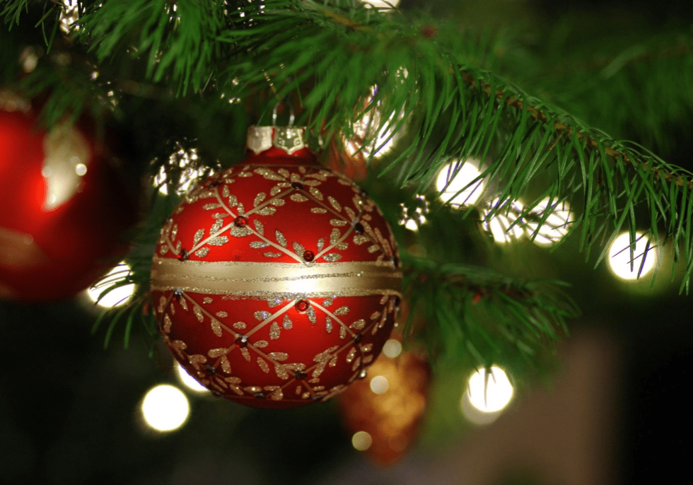 A red and gold ornament hanging from the top of a christmas tree.