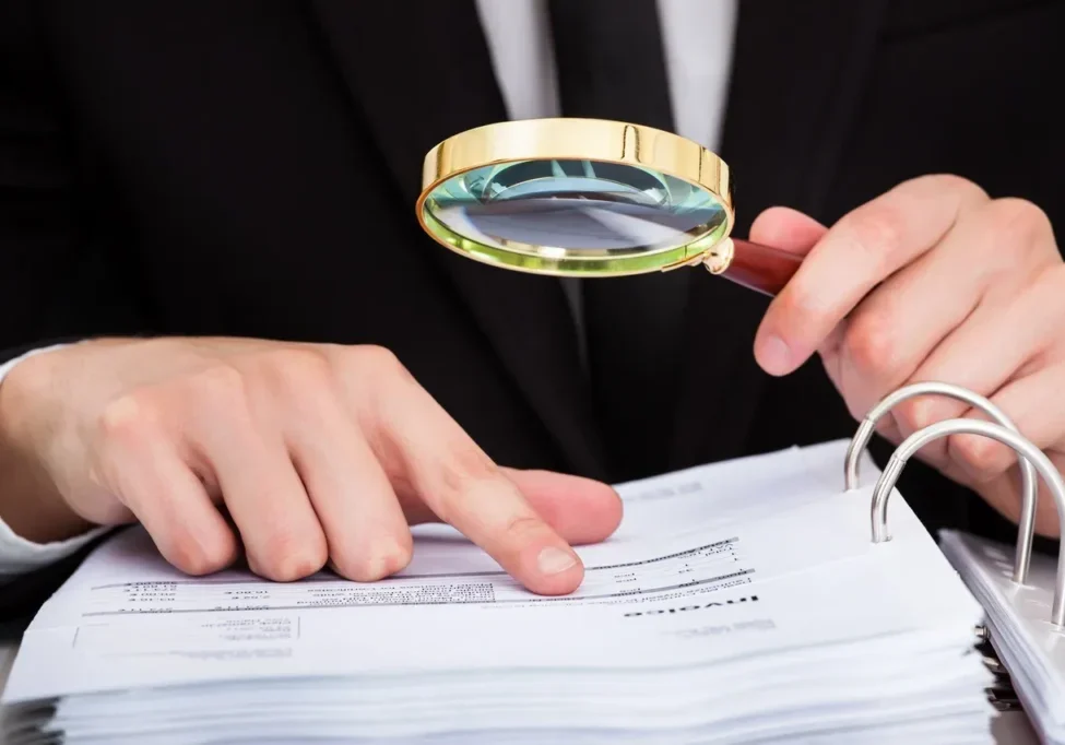 A person with a magnifying glass looking at papers